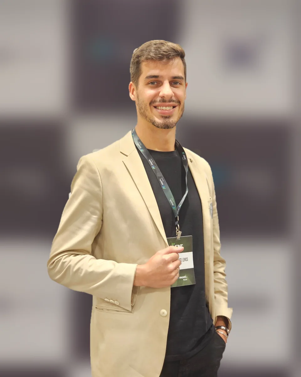 Guto Lemos de blazer bege, sorrindo, em um evento do mercado financeiro